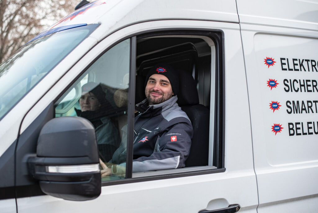Zwei Mitarbeitende im weißen Firmenwagen, rechts Text: ELEKTRO, SICHER..., SMART..., BELEU...