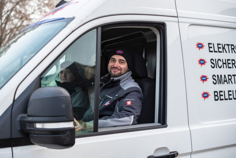 Zwei Mitarbeitende im weißen Firmenwagen, rechts Text: ELEKTRO, SICHER..., SMART..., BELEU...