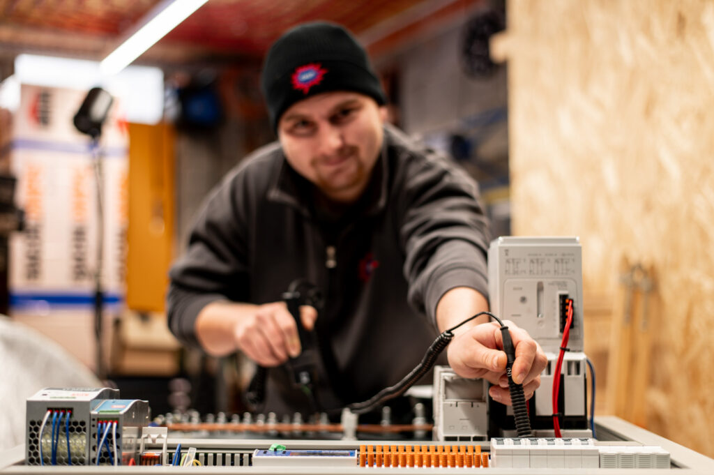 Techniker prüft Schaltschrank, vorne Netzteile und Klemmen, rechts offenes Modul mit Kabeln in Werkstatt